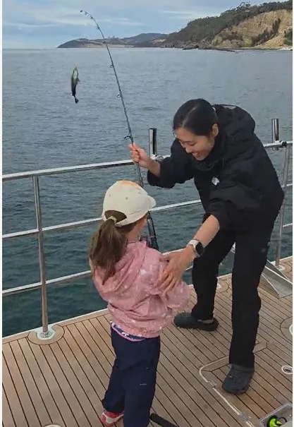 Young girl reeling in a fish from the deck of a charter boat off the coast of Hobart, Tasmania
